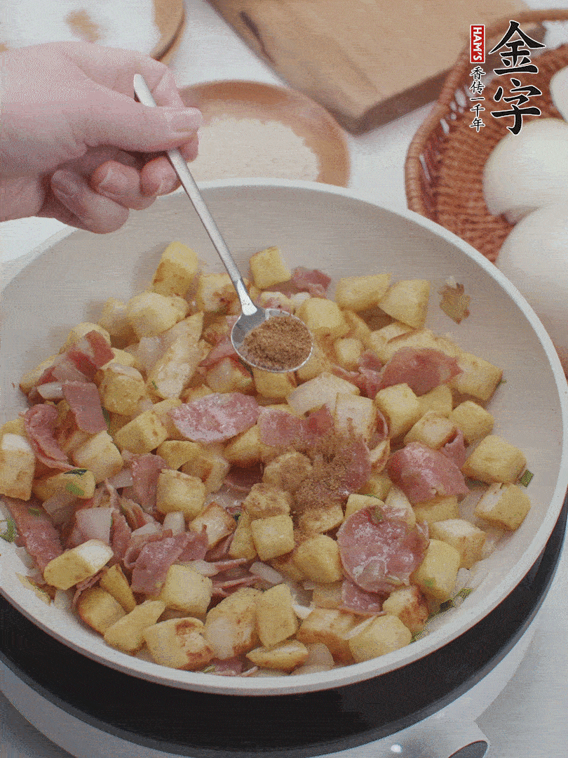 起鍋少油，煸香洋蔥丁、蔥白，加入金字培根火腿翻炒幾下，再加入饅頭丁、1小勺孜然粉、少許鹽翻炒均勻并鋪平。